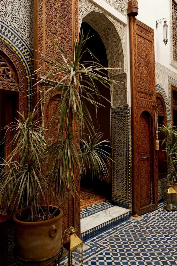 A leafy courtyard corner with carved doors and mosaic decoration